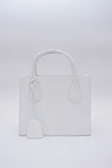 Cartera mediana de cuero blanco, con asa fija y correa regulable desmontable.
