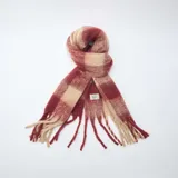 Bufanda de tejido suave con diseño de cuadros grandes en tonos rojo y beige, terminada con flecos en los extremos.