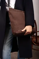 Bolso tipo bucket de gamuza color violeta con correa ajustable de cuero negro y detalles de costuras pespunteadas a la vista.