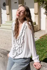 Blusa rosada de manga larga con escote en V, volados frontales con ribete negro contrastante y puños elásticos.