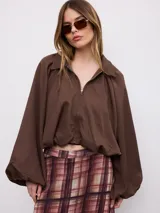 Campera marrón de mangas murciélago abullonadas, con cuello camisero, cierre frontal y ajuste elástico en el ruedo.