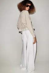 Chaqueta de punto color beige con cuello redondo, manga larga y cierre frontal con botones. Presenta un diseño combinado con volados de tela en el bajo.