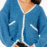 Cardigan de tejido peludo en color azul con detalles de borde en contraste color celeste claro. Presenta escote en V, cierre frontal con botones y dos bolsillos delanteros.