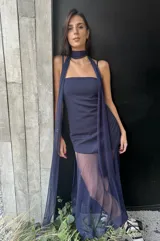 Vestido largo de color azul marino con base de crepé asimétrica y sobrecapa de microtul translúcido. Presenta un diseño de escote recto sin breteles y falda con transparencia. Incluye un accesorio de tela a juego versátil para usar como chal o lazo al cuello.
