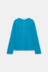 Camiseta turquesa oversize de manga larga y cuello panadero con cierre de botones en el pecho. Cuenta con dos bolsillos de parche delanteros.