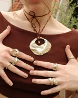 Collar artesanal con dije de bronce macizo en forma orgánica irregular, similar a una concha marina, suspendido de un cordón de seda natural negro. El diseño permite diversas formas de uso, ya sea ajustado al cuello o largo.