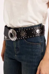 Cinto de cuero sintético negro con tachas metálicas plateadas y hebilla grande circular con detalle de piedra central negra y grabados ornamentales.