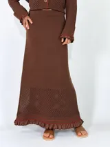 Pollera larga de punto color marrón, con diseño calado en el dobladillo y detalles de volados y costuras en tono rojizo.