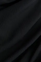 Vestido corto negro en punto texturizado, de corte entallado con hombros descubiertos, escote en V y frunces laterales que generan un efecto drapeado. Cuenta con un nudo ancho asimétrico al frente.