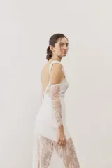 Vestido largo blanco de encaje con diseño asimétrico, tirante fino en un hombro y falda transparente.