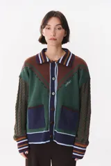 Cardigan de punto con diseño multicolor en tonos marrones, bordó y detalles en amarillo y celeste. Presenta cuello tipo polo, cierre frontal con botones, bolsillos aplicados en el frente y mangas con trama trenzada y coderas bordadas.