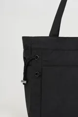 Bolso tipo tote bag color beige con asas superiores de hombro, cordones ajustables a los lados con detalles metálicos y un pequeño anillo frontal.