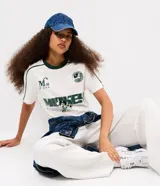Remera boxy de algodón color blanco, con cuello redondo y ribete verde oscuro, manga corta con líneas decorativas en los hombros, y estampado frontal deportivo de Mickey Mouse con tipografía.