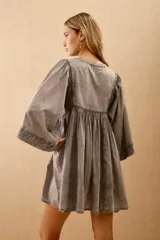 Vestido corto de algodón color gris lavado, con escote en V y cordones ajustables. Presenta mangas anchas tipo murciélago y bordados florales en el canesú.