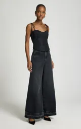 Jean wide leg negro de tiro alto con perneras anchas y dobladillo deshilachado, con bolsillos delanteros y traseros, y cierre frontal con botón metálico y cremallera.