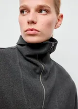 Jersey de cuello alto con cierre de cremallera corta y manga larga, de diseño amplio y color gris oscuro.