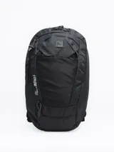 Mochila de trekking color negro, confeccionada en nylon ripstop. Cuenta con compartimento principal amplio, bolsillo frontal abierto, compartimento superior con cierre y pasadores exteriores para accesorios. Incluye tiras ajustables con broche frontal y cubre lluvia integrado.