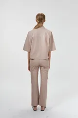 Camisa de cuero ovino color rosa pálido, de corte recto y estilo minimalista. Tiene mangas cortas, cuello clásico, cierre con botones a presión plateados y bolsillos delanteros con solapa.