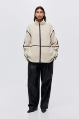 Campera de corte holgado confeccionada en tejido de sherpa suave, con cuello alto y cierre frontal. Presenta detalles de ribetes en contraste y diseño de hombros caídos.