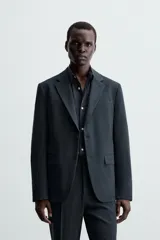 Blazer slim fit de color gris, confeccionada en tejido con lana. Presenta cuello con solapas de muesca, cierre frontal con un botón, bolsillos de solapa en la cadera y bolsillo de vivo en el pecho.