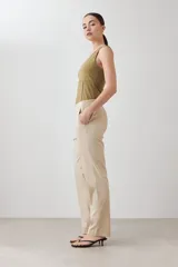 Pantalón de corte recto y tiro medio, confeccionado en tela de gabardina color beige. Presenta cierre frontal con cremallera y botón oculto, bolsillos laterales y costuras verticales decorativas en la parte superior.