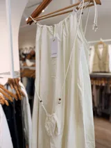 Vestido midi celeste de silueta amplia y fluida, con escote fruncido y tirantes finos decorados con cuentas de madera. Incluye una pequeña carterita colgante haciendo juego.