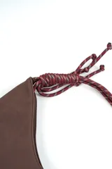 Cartera tipo hobo de gamuza color marrón, con costura central vertical y correa de cuerda trenzada en tonos borró y gris con nudos decorativos en los extremos.