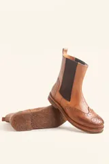 Bota tipo Chelsea de cuero vacuno color suela, con diseño brogue en la puntera y laterales. Presenta paneles elásticos laterales en color marrón oscuro, tirador trasero y suela de goma con plataforma.
