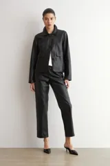 Chaqueta de eco cuero negro con cuello camisero, cierre frontal oculto y mangas largas con puños rectos.