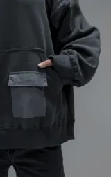 Hoodie oversize de algodón con diseño bicolor en gris oscuro y gris medio. Presenta capucha forrada, mangas raglán con recortes técnicos y un bolsillo frontal tipo canguro con un compartimento adicional con solapa.