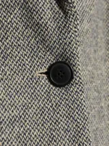 Blazer gris con diseño de espiga, solapas con muescas y cierre con un botón.