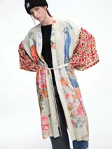 Kimono largo de rayón con diseño artístico estampado que combina motivos florales y figuras de aves. Presenta mangas amplias con detalles en contraste y corte abierto frontal.