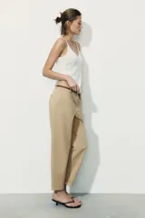 Pantalón chino color beige de tiro medio con bolsillos frontales y falsos bolsillos de vivo en la espalda. El bajo tiene un acabado con vuelta. Incluye un cinturón trenzado marrón.