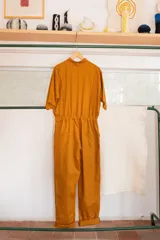 Mono color ocre de gabardina 100% algodón, con corte clásico, cierre frontal completo, pantalón largo con bolsillos, manga corta y cintura fruncida en la espalda.