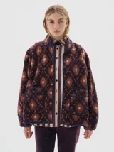 Campera de sherpa con estampado geométrico en tonos bordó y rosa, cuello alto, cierre frontal con broches a presión y bolsillos frontales con ribetes en contraste.