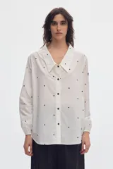 Camisa oversize blanca con estampa de lunares negros, cuello en pico con solapas clásicas y mangas abullonadas con puños elásticos.