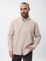 Camisa de manga larga en algodón tramado, con cuello clásico abotonado y cierre frontal con botones. Presenta un diseño liso con textura visible y un pequeño bordado en la pechera.