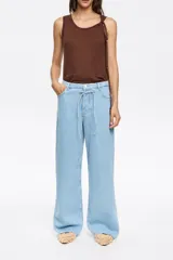 Pantalón largo de jean, color celeste claro, con corte wide leg y tiro bajo. Presenta cierre frontal con botón, cinco bolsillos y cordón ajustable en la cintura.