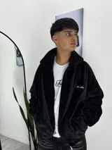 Campera de corderoy negro con cierre frontal, cuello alto y bordado decorativo en el pecho. Presenta un diseño holgado con bolsillos laterales.