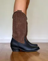 Botas texanas de caña alta confeccionadas en cuero negro, con costuras decorativas en contraste color ocre en la caña y taco cuadrado de madera.