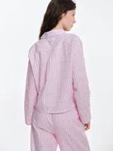 Camisa de dormir de popelina de algodón, con estampado de rayas verticales y pequeños motivos geométricos. Presenta cuello camisero, mangas largas y cierre frontal mediante lazos ajustables.