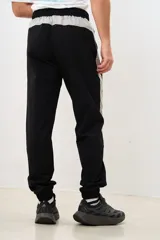 Pantalón negro de corte deportivo con cintura elástica y cordón ajustable. Presenta una franja vertical gris a lo largo de la pierna y puños elásticos.