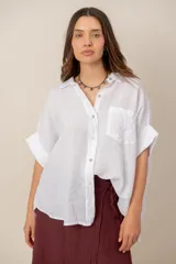 Camisa de lino blanca de manga corta, corte holgado, con cuello camisero, cierre frontal con botones y un bolsillo en el pecho con detalle bordado.
