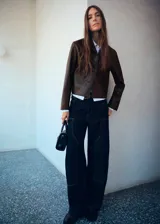 Chaqueta corta de efecto piel en color marrón chocolate, con cuello camisero, cierre frontal con botones y dos bolsillos de parche delanteros.