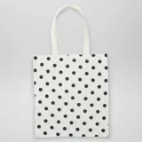 Tote bag de tela color blanco con estampado de lunares negros y asas de hombro blancas.