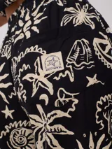 Pantalon de corte recto y holgado, confeccionado en algodón estampado con motivos playeros como palmeras, soles y caracoles en color crema sobre fondo negro. Posee cintura elástica.