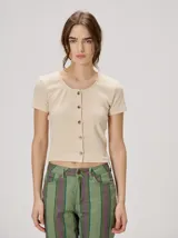 Remera corta de color beige, confeccionada en tejido elastizado, con cuello redondo y cierre frontal de botones.