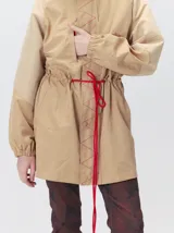 Campera tipo piloto con capucha, cierre frontal con botones y detalle de costuras en zigzag. Presenta cordones ajustables en la cintura y capucha, puños elásticos y logo bordado en el pecho.