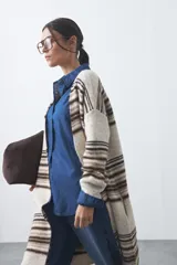 Cardigan largo de tejido de punto con diseño de rayas horizontales en tonos beige, marrón y blanco. Presenta una silueta relajada, mangas largas y frente abierto.