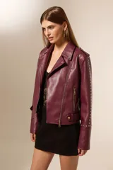 Chaqueta tipo biker color borgoña de cuero sintético con tachas plateadas en hombros y mangas, cierre asimétrico y cuello solapa.